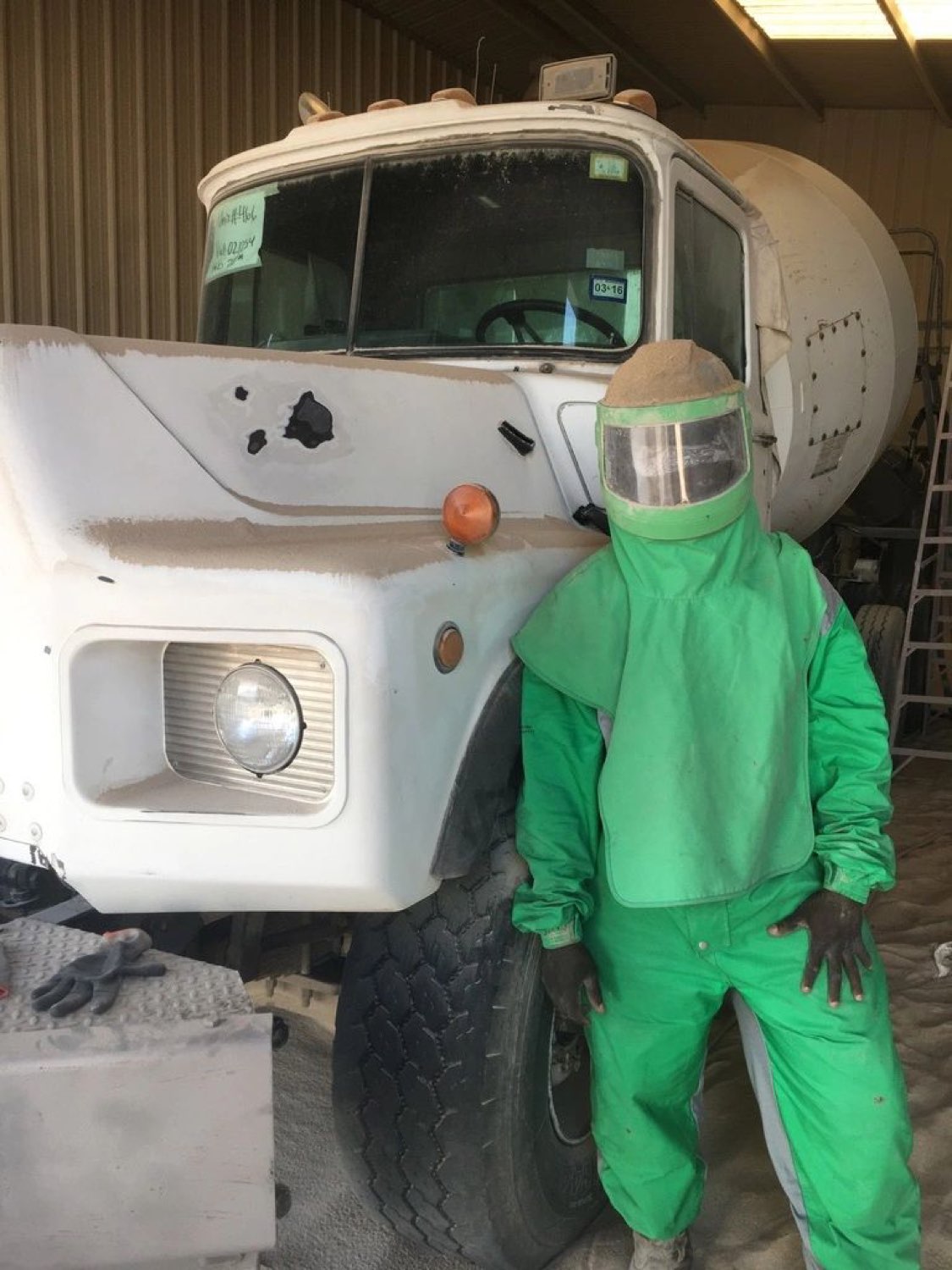 A SuperMixers technician in protective gear beside a mixer truck cab stripped back to bare steel