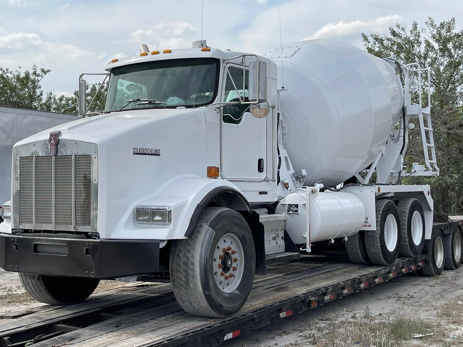 A Kenworth mixer truck loaded on a lowboy trailer for transport